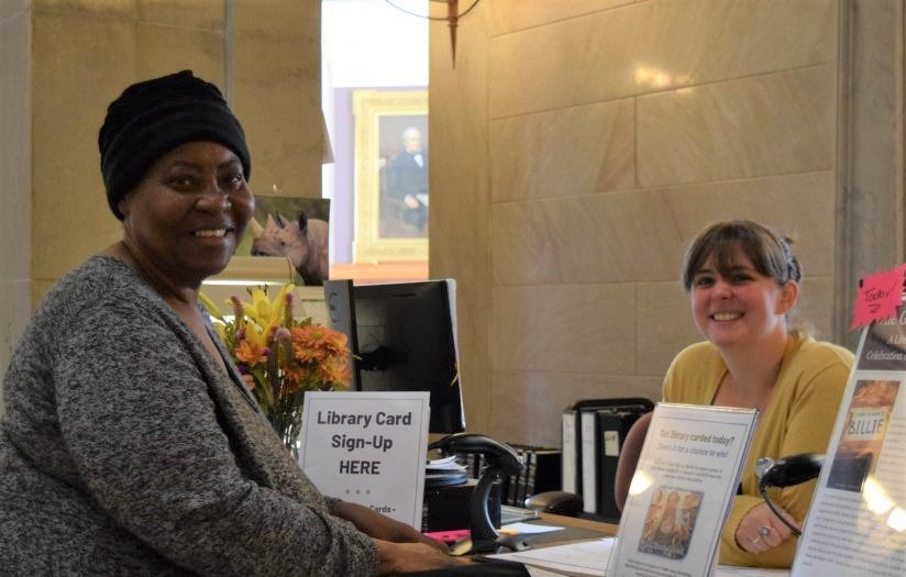 A patron and librarian smiling at the circulation desk.